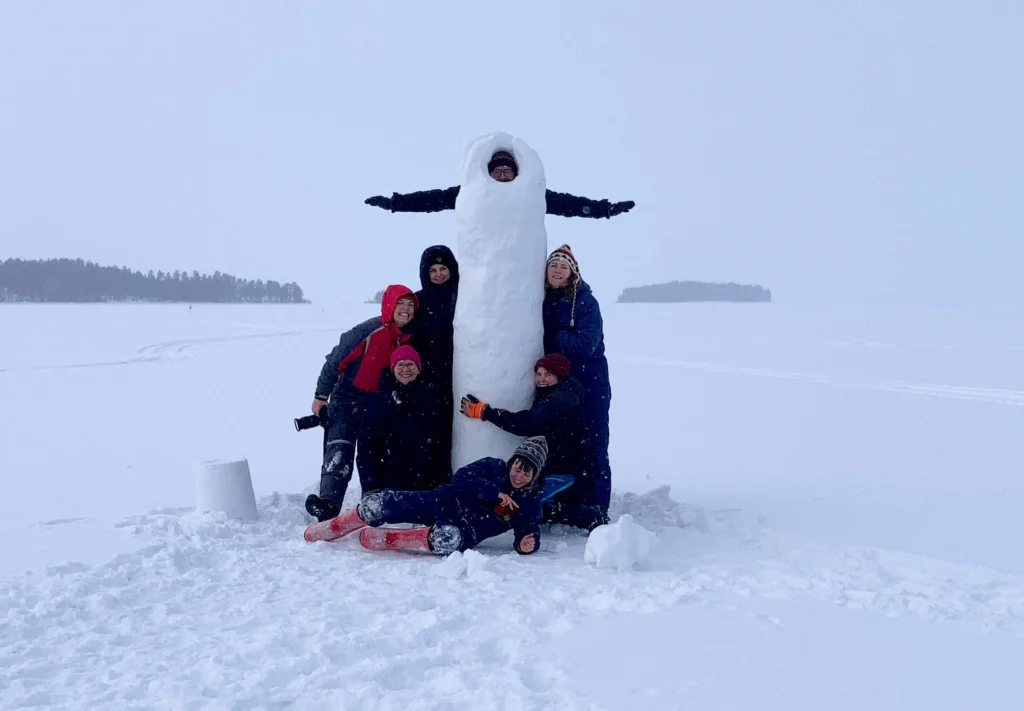 monta ihmistä seisoo korkean lumiveistoksen vierellä talvisessa maisemassa